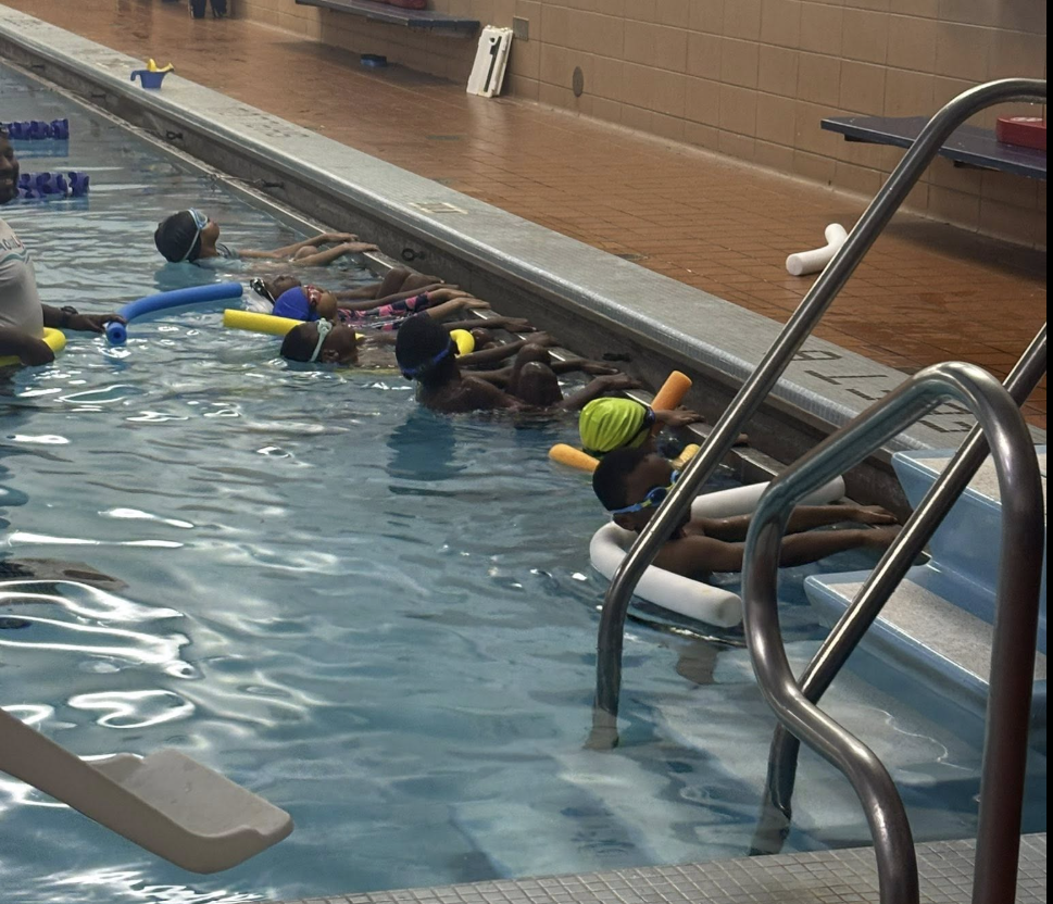 Children learning to swim with foam noodles in a pool during a foundation swim class